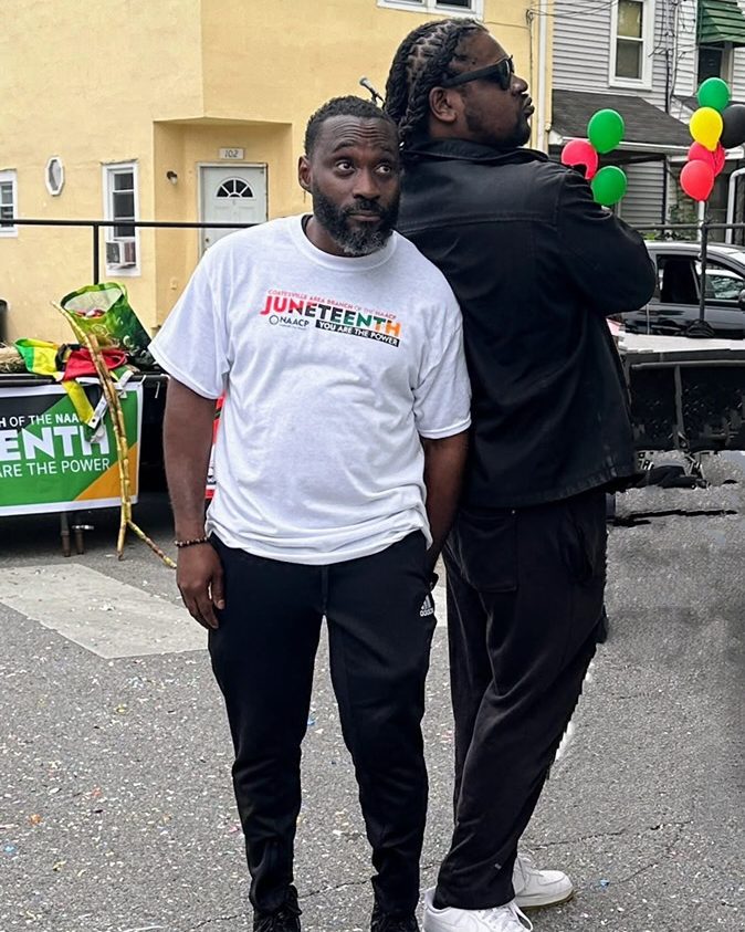 Ajené in a Coatesville Area Branch NAACP Juneteenth shirt at the Freedom Celebration, balloons in red, black, and green behind him.