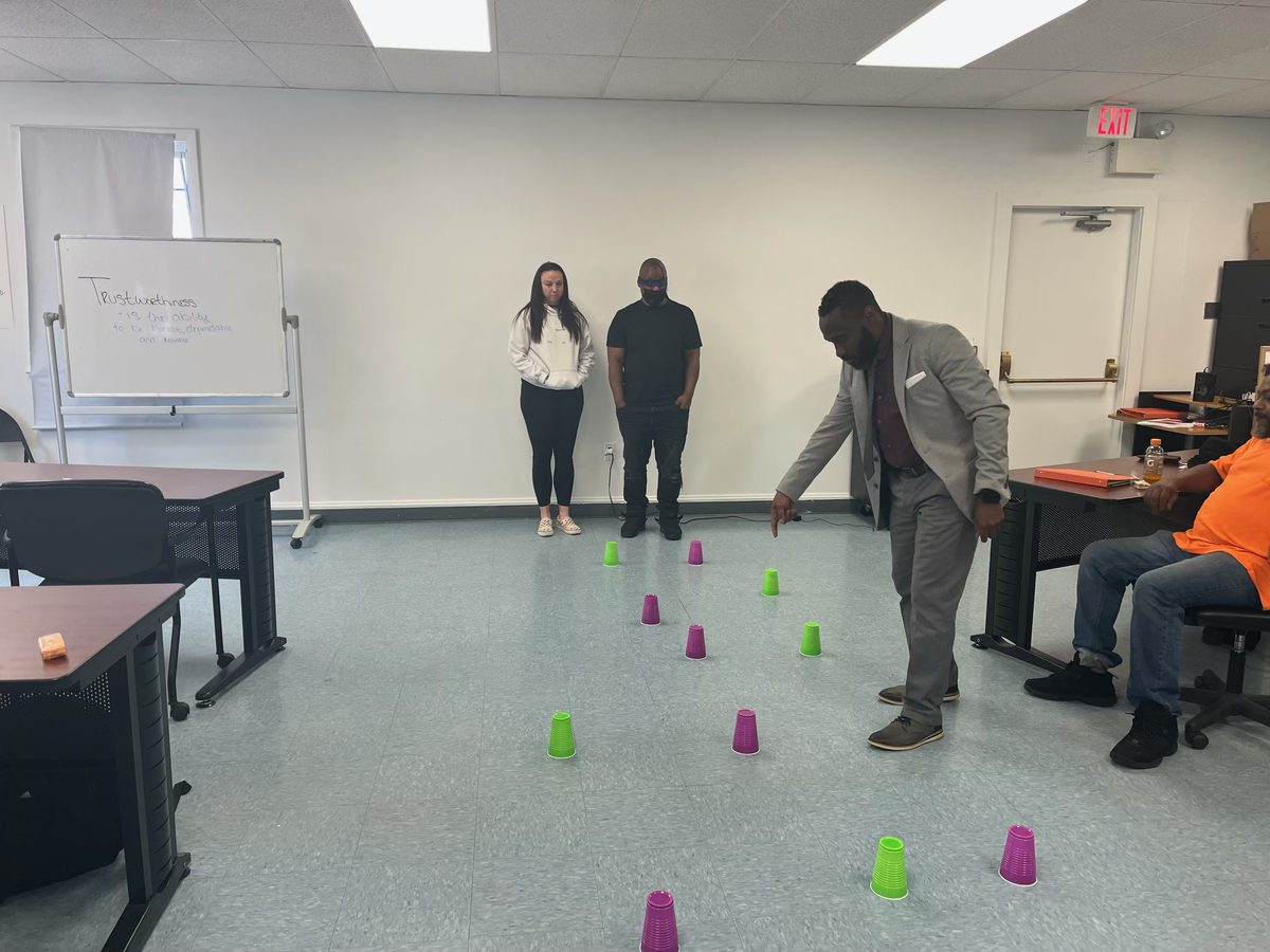 Ajené leading a trust exercise with Work Enclave participants in a training room.
